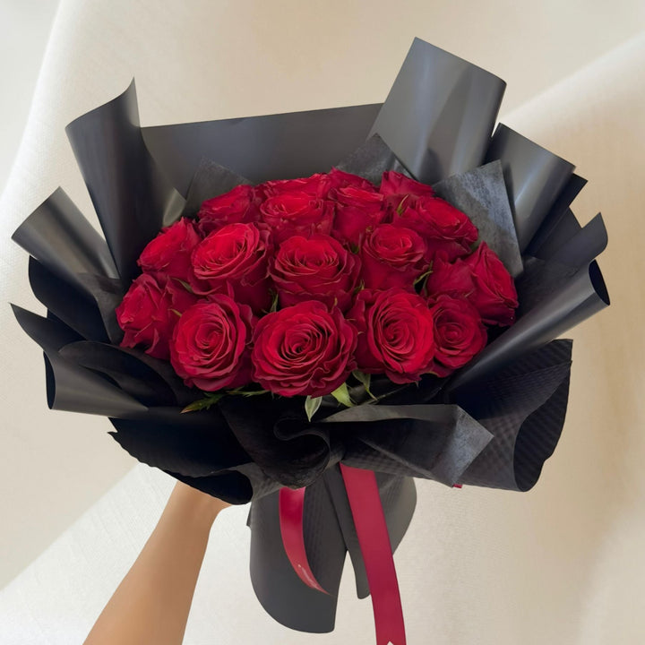 A bouquet of red roses wrapped in black paper with a red ribbon.